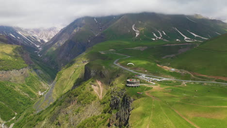 wide drone shot of paraglider flying near the arch of friendship of peoples in gudauri georgia