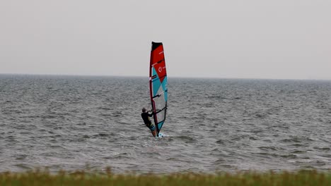 wind surfer heading out to sea from the shoreline on an overcast stormy day in pattaya, thailand