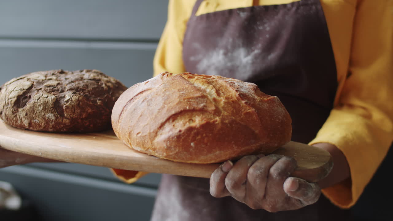 manos de una panadera negra sosteniendo un tablero con pan fresco