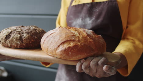 hands of black female baker holding board with fresh bread