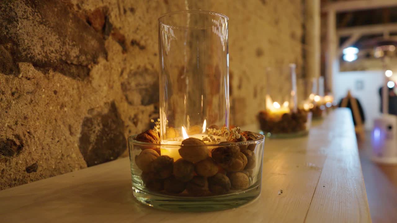 Row of glass candle holders with nuts on white ledge by stone wall