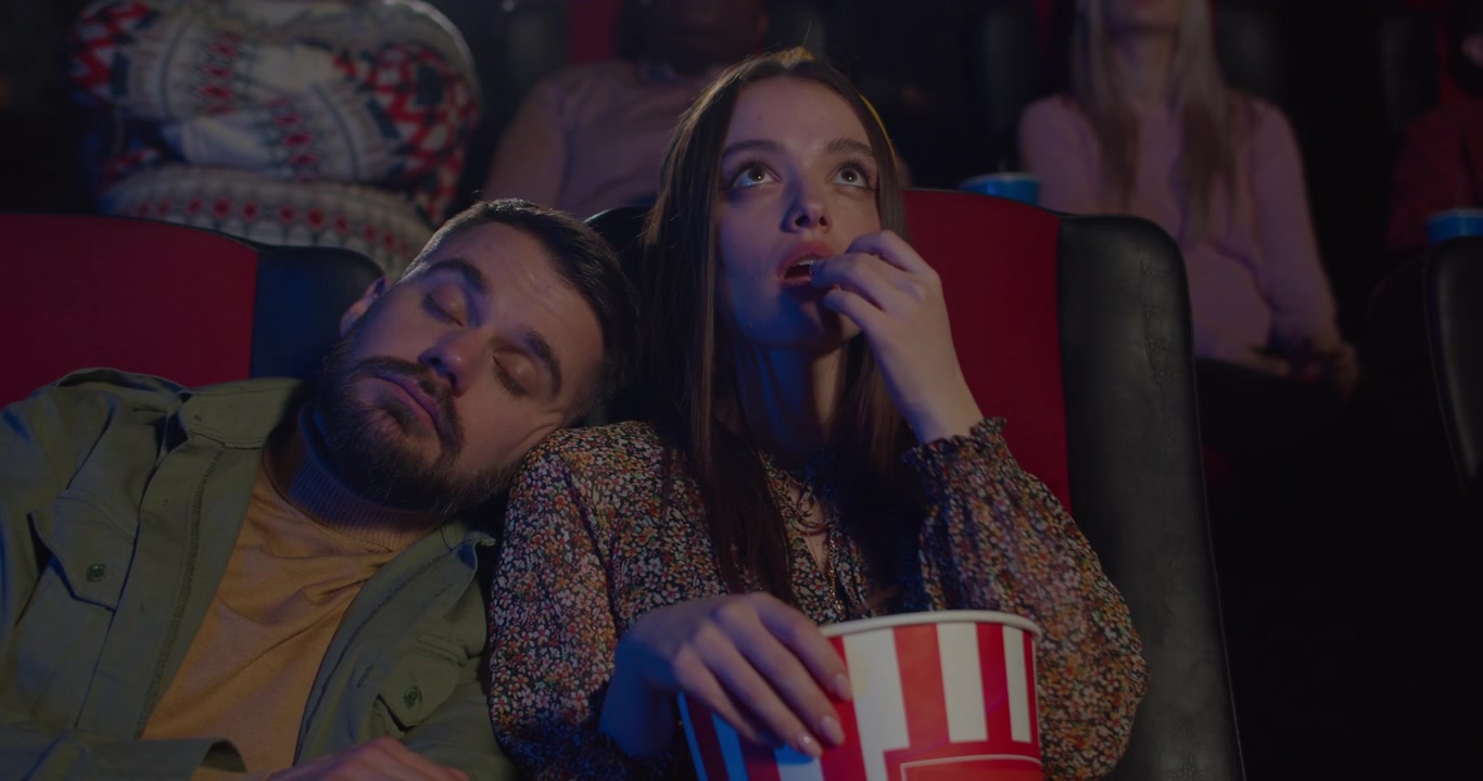 Jovem Mulher Comendo Pipoca Enquanto Homem Dorme em Seu Ombro no Cinema.