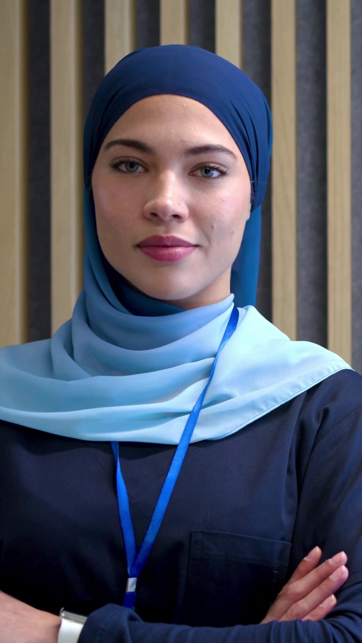 Vertical video: Blinking, woman smiling for badge by slat wall with lanyard, hijab, wrist device
