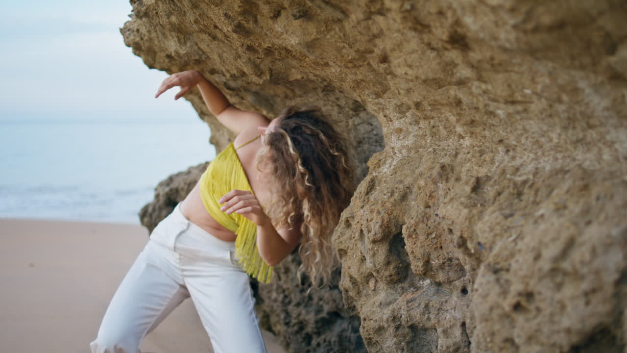 Jovem moderna dançando na praia de areia em um dia de verão. Mulher sensual em movimento.