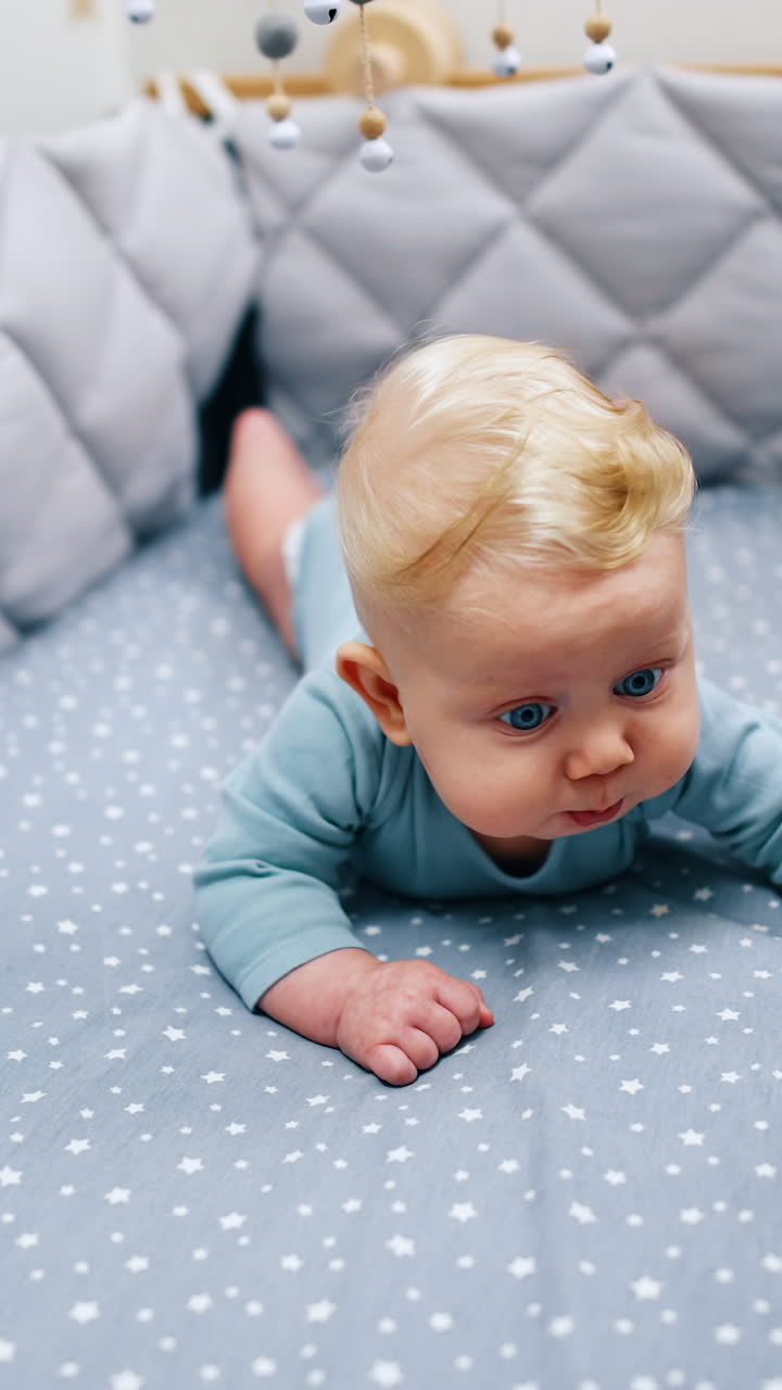 Lovely cute child lying on the belly in the blue crib. Cot mobile is hanging above the baby boy. Vertical video