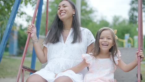 a pregnant mother and her young daughter enjoy playful time together at a playground in the park, surrounded by trees and greenery