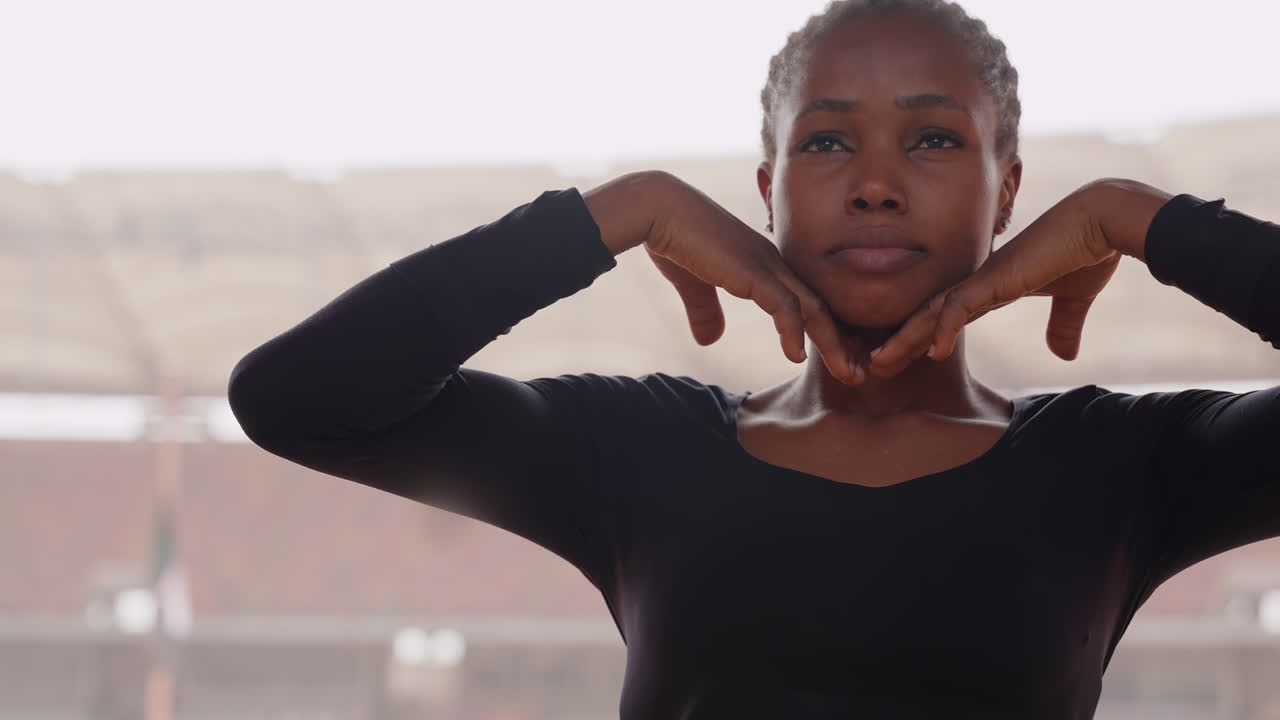 black woman dancer stadium warmup poised and expressive. Contemporary performer rehearses choreographed hand gestures and fluid posture under soft sunlight in empty arena stands focused training