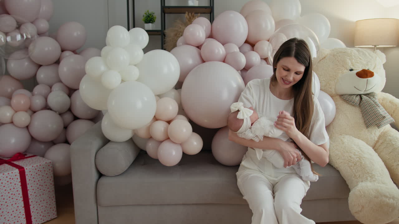 Madre sosteniendo a un bebé recién nacido rodeada de globos pastel y decoración de guardería con ositos de peluche para un baby shower