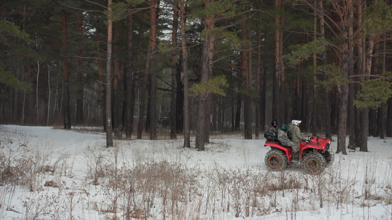 ATV rosso parcheggiato in una foresta innevata, un quad solitario che riposa tra alti pini, leggera nevicata che spolvera il terreno ghiacciato, tracce di pneumatici che conducono in boschi in ombra, luce fredda e smorzata che crea un ambiente calmo e remoto.