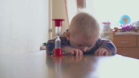 el niño se para en la mesa y la mamá le da un vidrio de arena en la habitación.