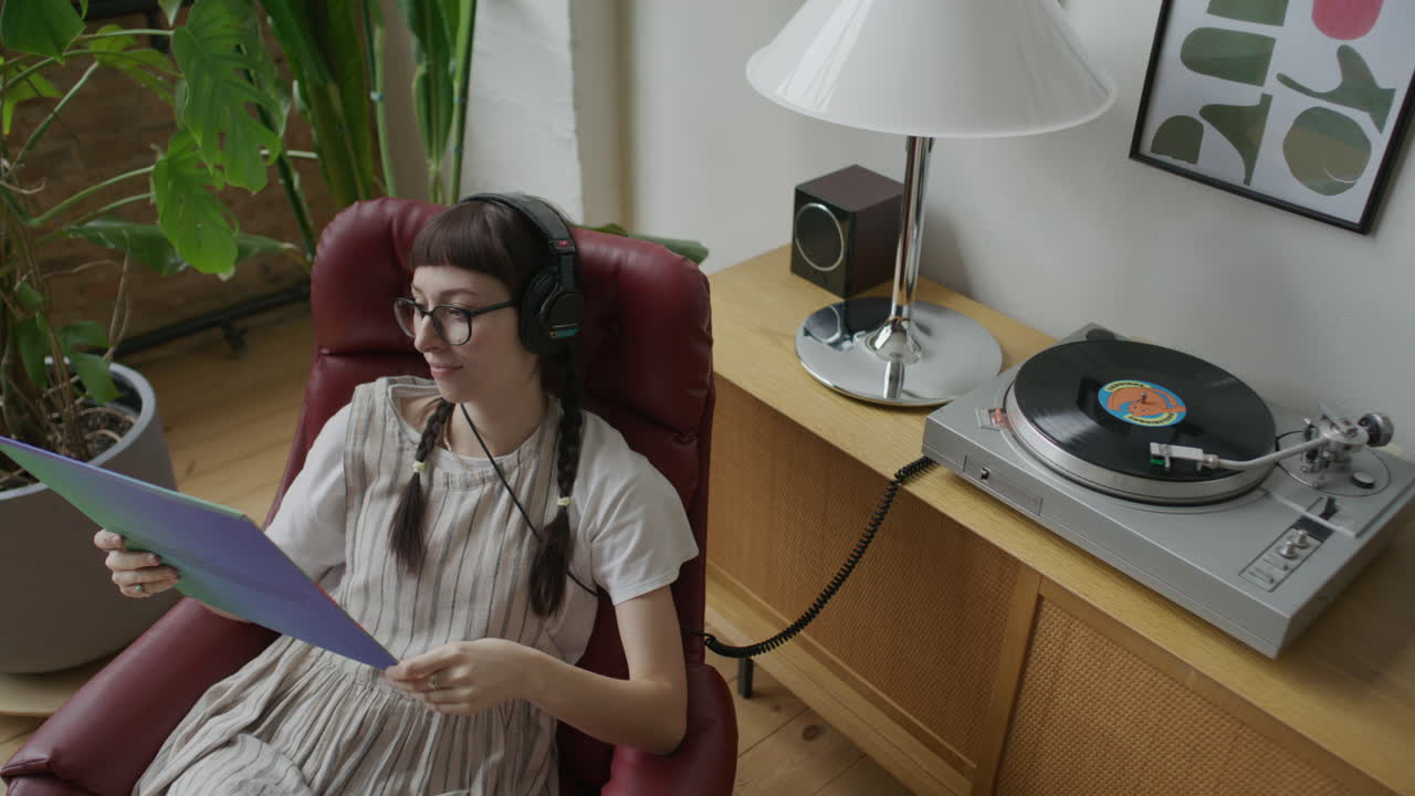 ターンテーブルで音楽を聴きながらレコードジャケットを読む若い女性