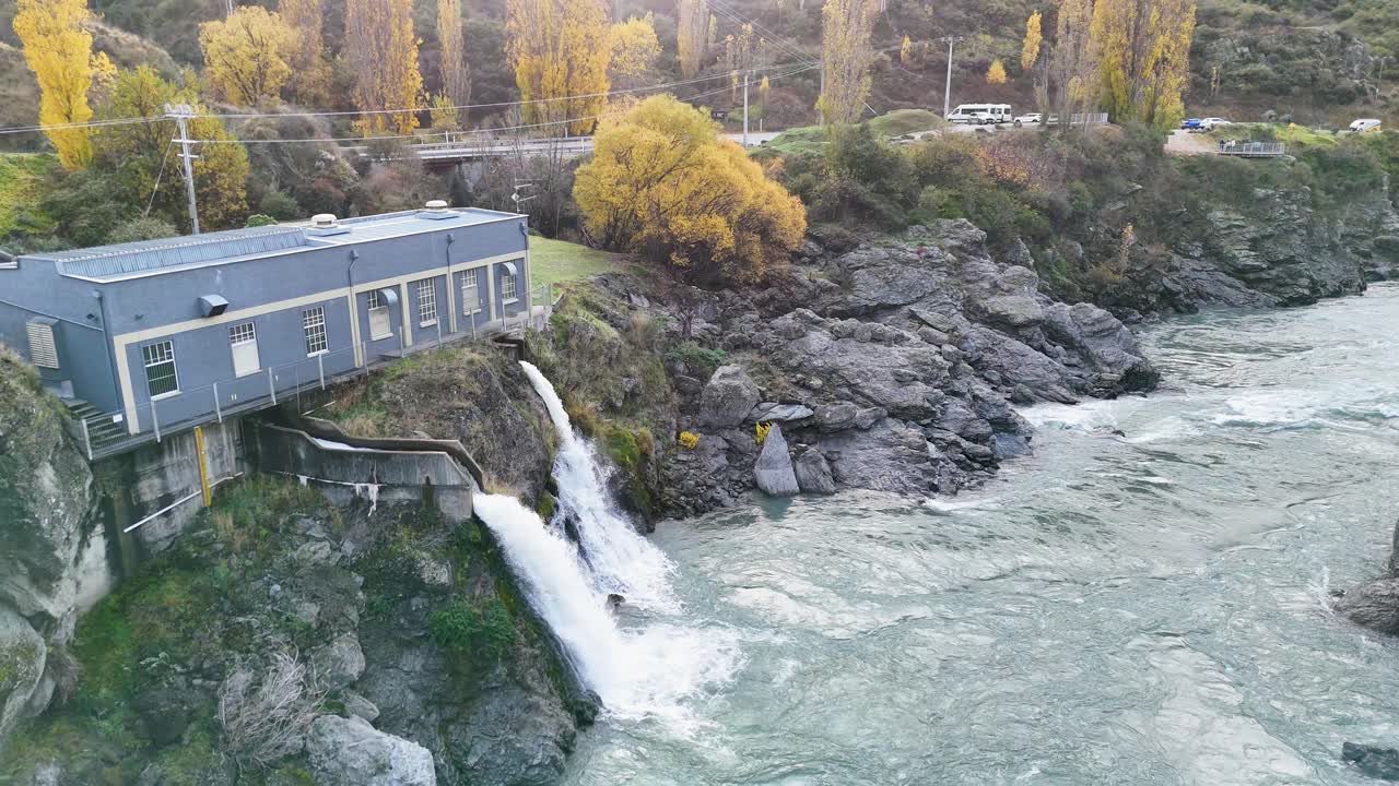 Drone footage captures the hydroelectric power station by Kawarau River, surrounded by autumn foliage in Queenstown, New Zealand
