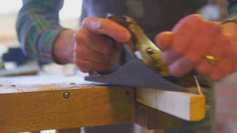 primer plano de un carpintero masculino en un taller de garaje planeando un pedazo de madera