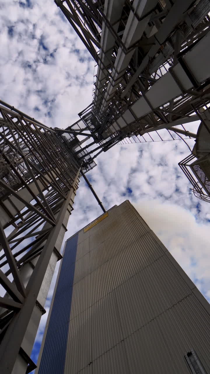 Industry. High metal stairs on the industrial plant. Modern territory for grain storage. Steel frame on warehouse outdoors. View from below. Vertical video