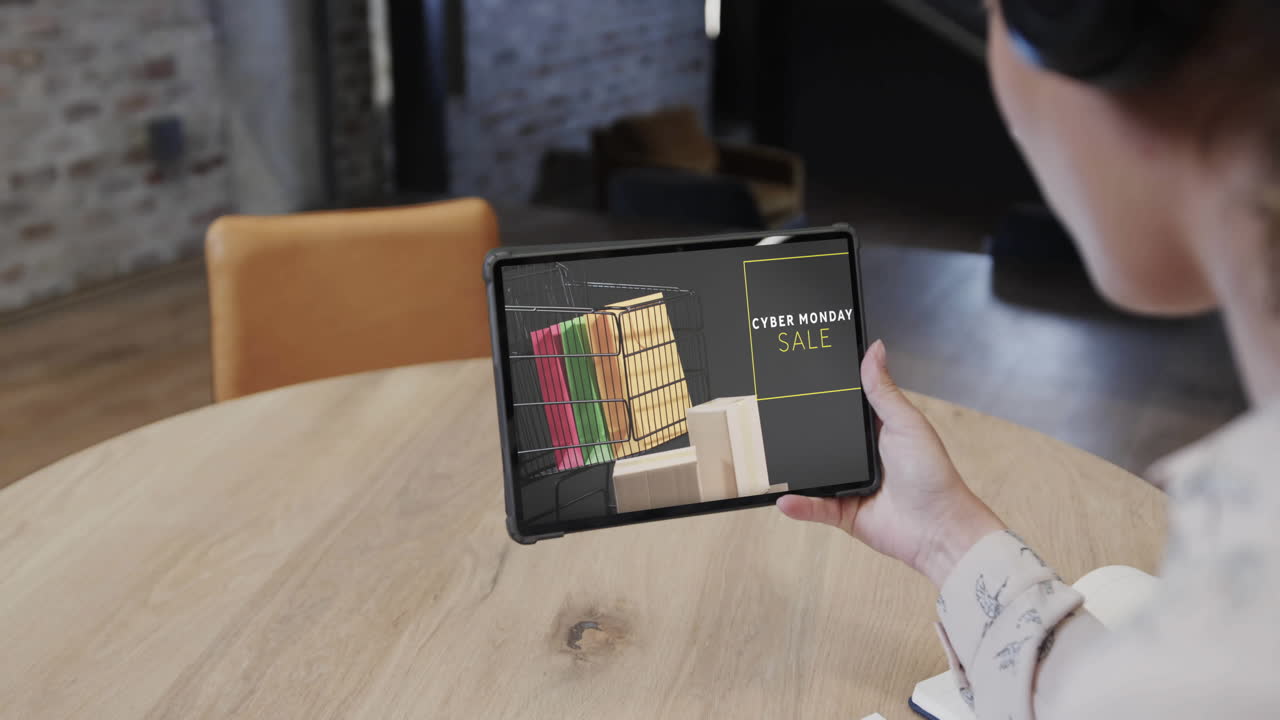 mujer biracial usando tableta en una cafetería comprando en línea en el día de venta del lunes cibernético, cámara lenta