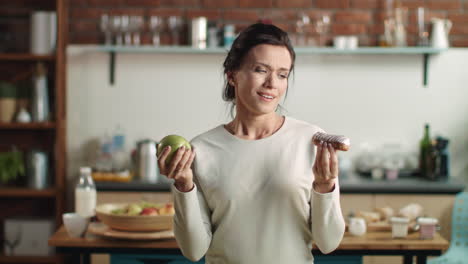 Frau-Schaut-Zwischen-Apfel-Und-Eclair.-Brünettes-Mädchen,-Das-Zu-Hause-Leckeren-Kuchen-Isst.