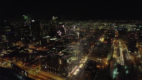 aerial drone flying through exploding fireworks show over downtown city skyline at night