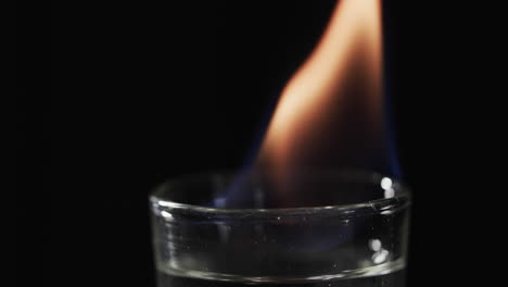 video of lit alcohol in glass with orange fire flame and copy space on black background