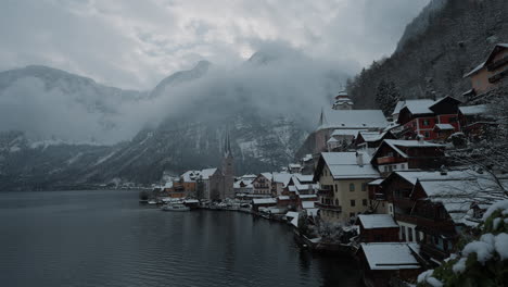 Snowy-day-in-Hallstatt,-Austria,-showcasing-snow-covered-rooftops,-mountains,-trees,-and-water-views-in-the-Austrian-Alps