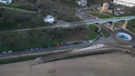 paralaje tiro aéreo de un pie de metal sobre un puente sobre una carretera concurrida con coches estacionados a un lado de ella en la bahía de scarborough, inglaterra