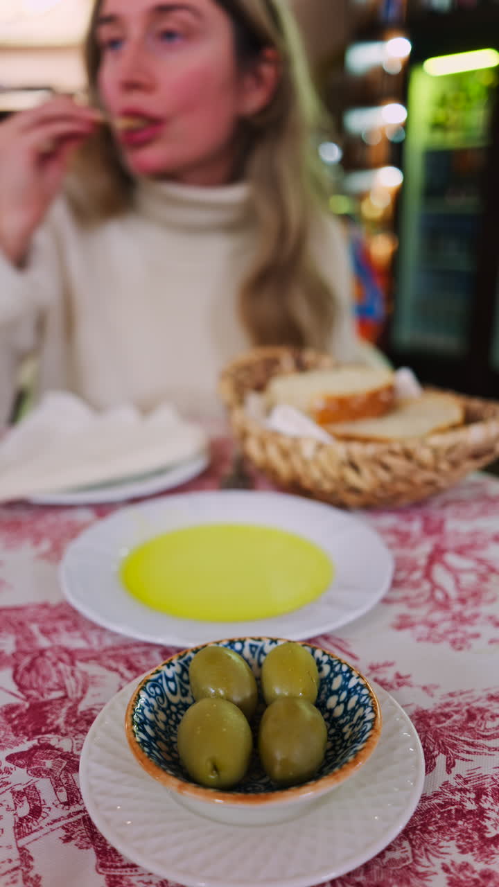 Close up of a woman dipping bread in olive oil and eating it at a restaurant. Vertical