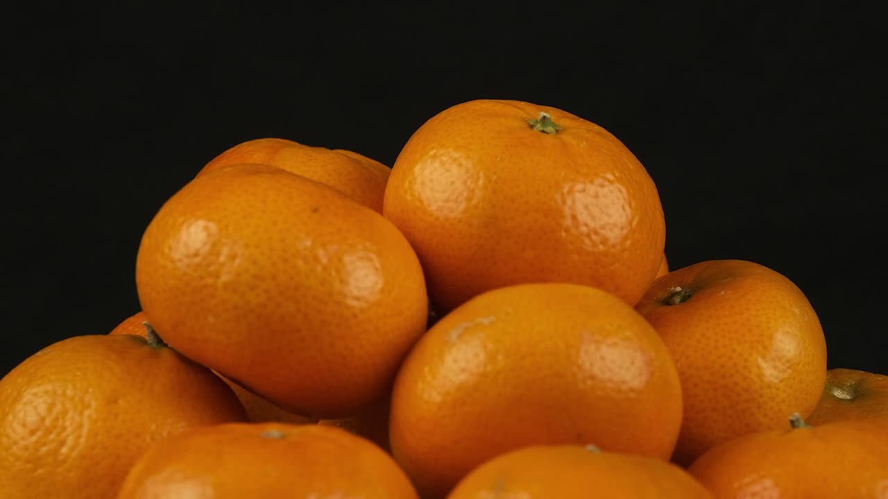 una pila de naranjas clementinas de mandarina gira sobre un fondo negro