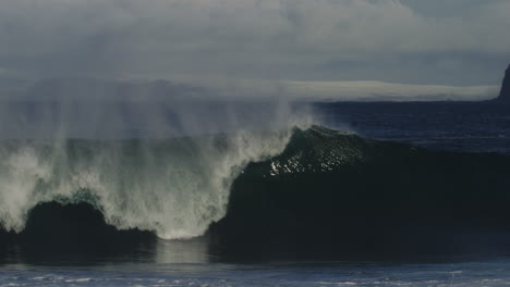 mist rises as lip of ocean wave crashes down, huge cliffs of ireland stand high in distance, slow motion