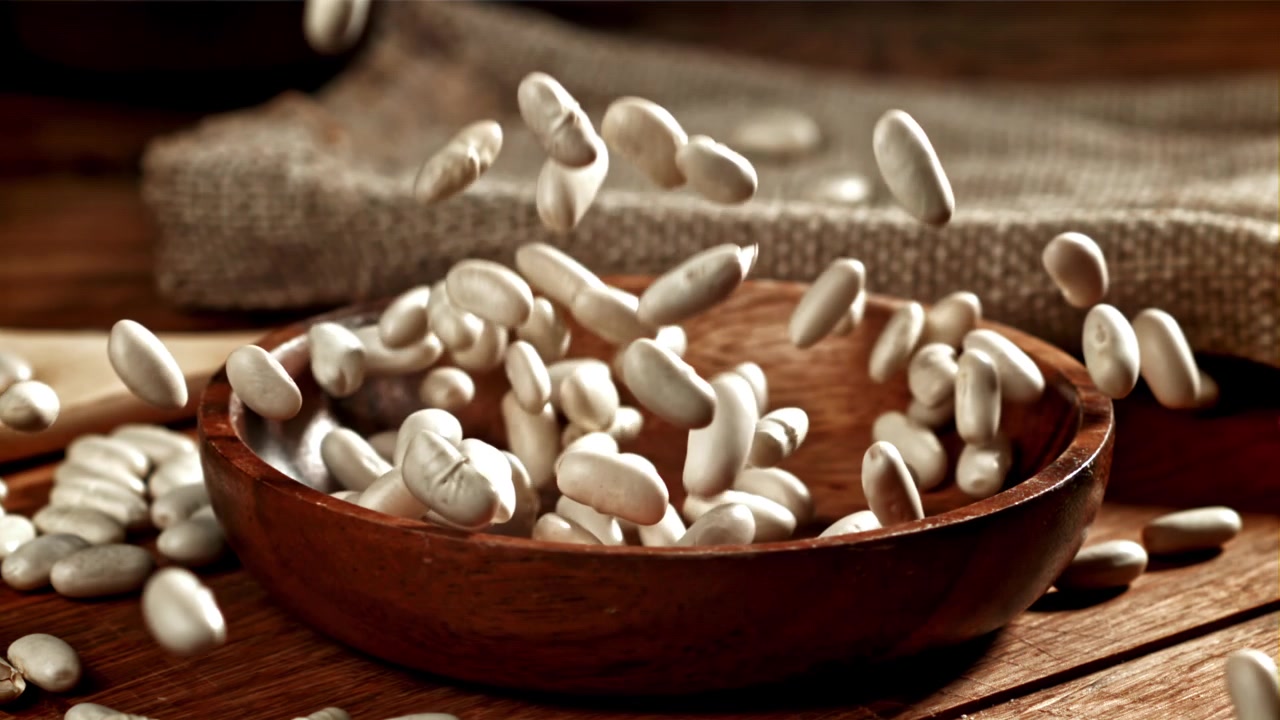 White Beans Falling into a Rustic Wooden Bowl in Slow Motion