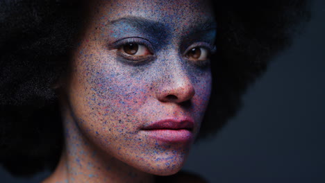 retrato de cerca de una hermosa mujer afroamericana que usa pintura exótica para la cara arte corporal mujer misteriosa con maquillaje colorido luz parpadeante en fondo oscuro concepto de expresión creativa