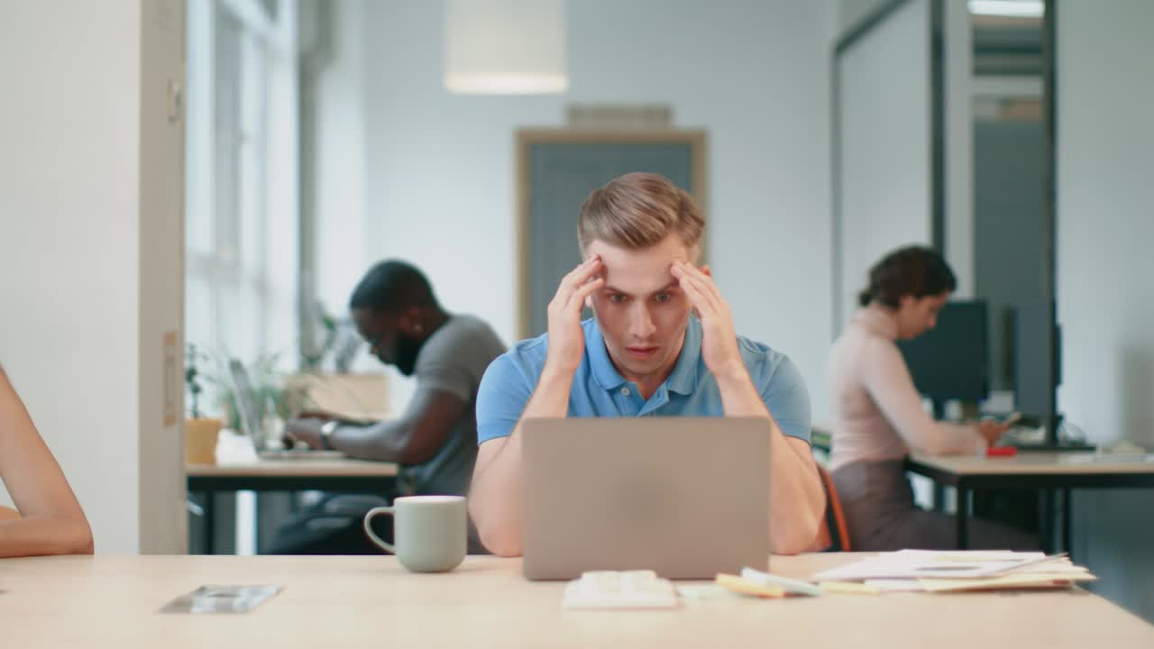 Serious man watching computer at workplace. Male person reading shocked news