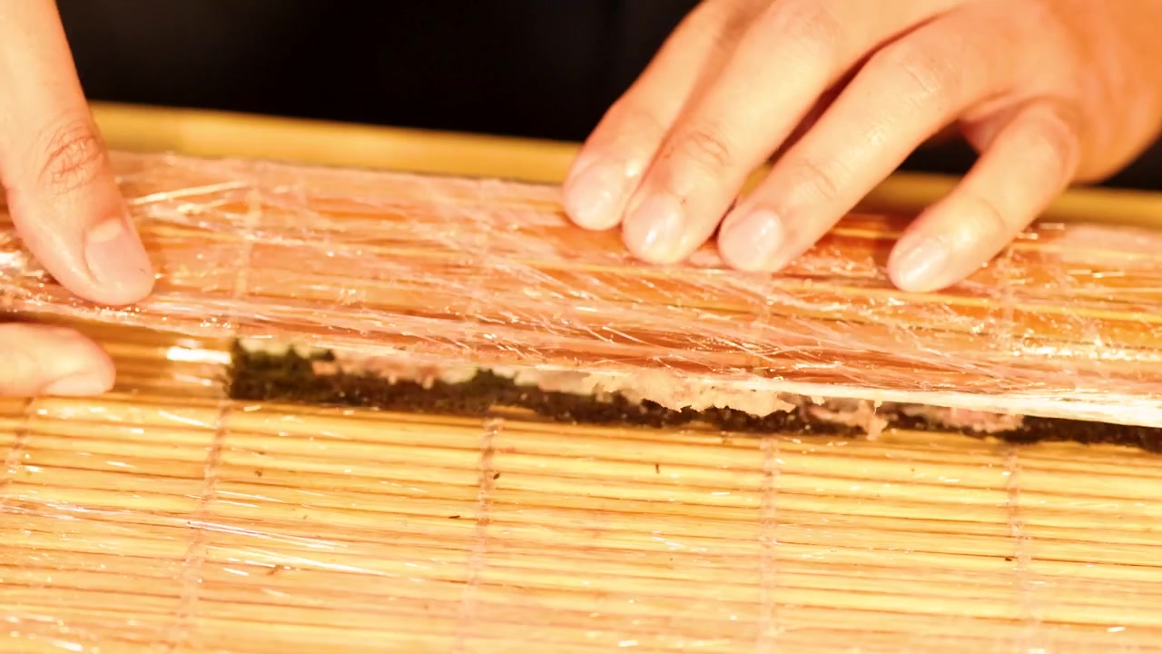 Detailní záběr rukou rolujících čerstvé tuňákové maki sushi pomocí tradiční bambusové podložky.