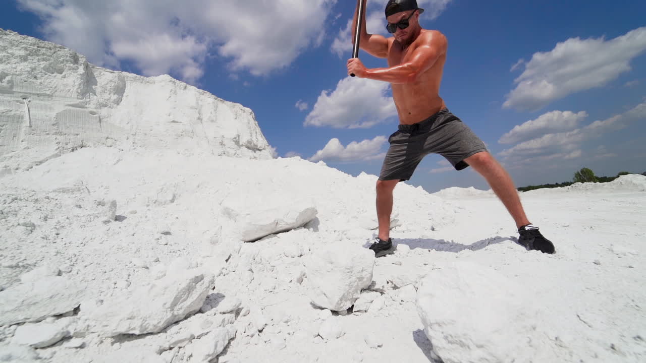 Muscular sportsman working in nature. Strong man with metal hammer breaking white rock on the mountain.