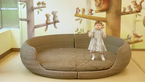 happy little girl jumping on rattan sofa in gyeonggi children's museum, south korea - wide shot