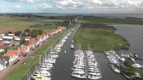 aerial pan showing the port area for pleasure boats and sailboats with typical houses of the dutch village of durgerdam at the durgerdammerdijk with clouds casting shadows in the landscape