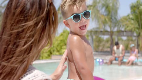 madre caucásica feliz usando crema solar en su hijo en la piscina