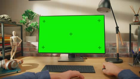 pov first person view of a man working on desktop computer with green screen mock up display. male sitting at a desk, browsing internet and using mouse at home in stylish living room.