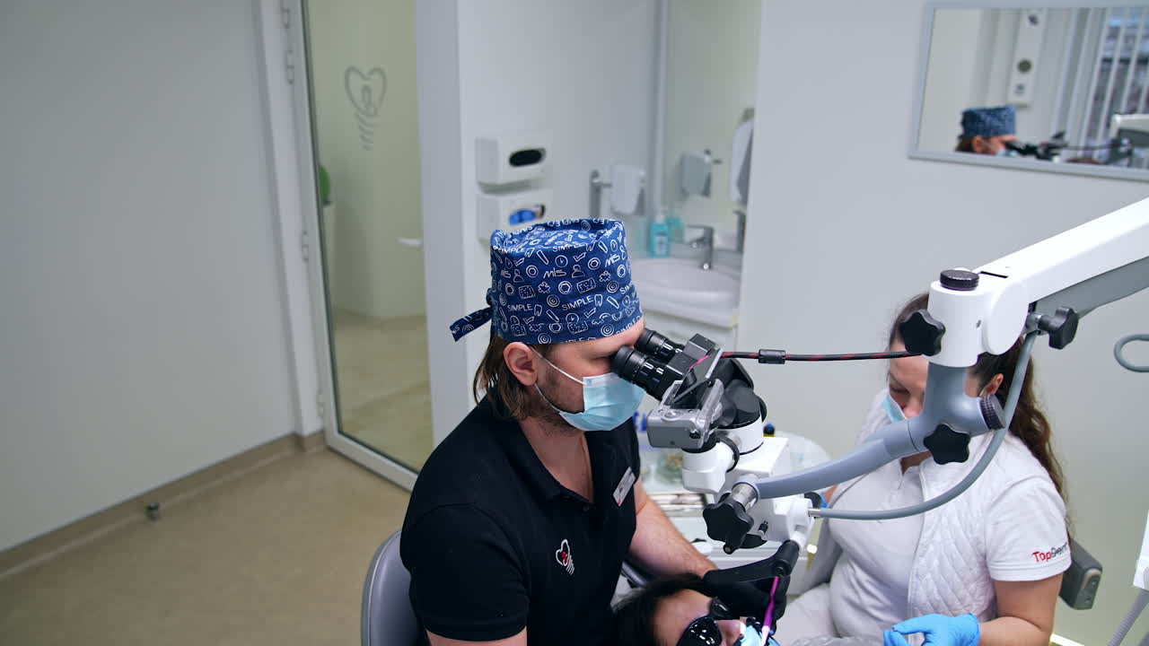Dentist using technological equipment in the dental practice. Doctor sits looking into microscope and performing procedure in the patient's mouth. View from top.