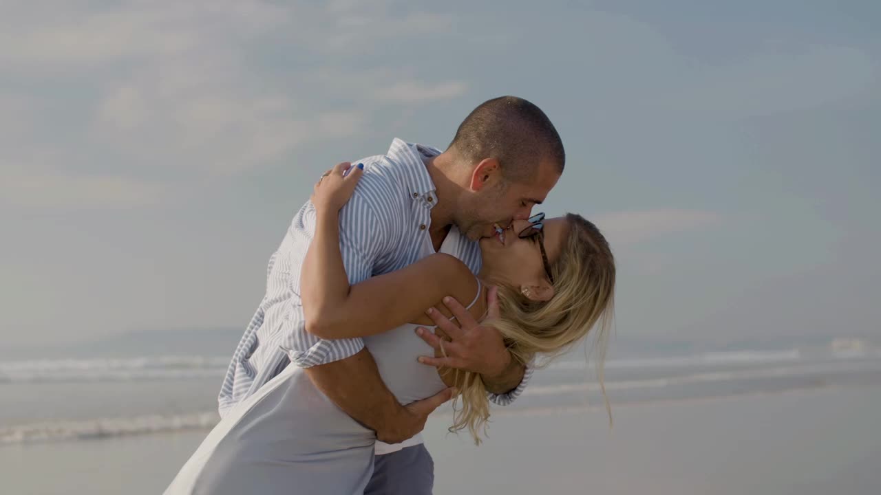 una pareja caucásica enamorada besándose en la orilla del mar, caminando al atardecer.