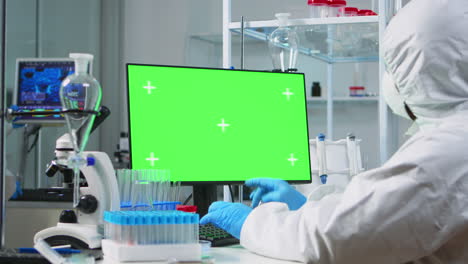 médico con traje de protección escribiendo en la computadora con una maqueta verde