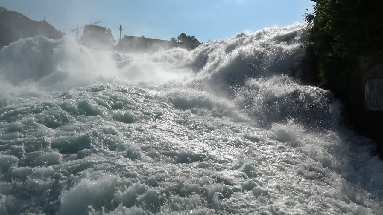 Dramatic view of Rhine Falls with foaming whitewater rapids and spray in sunlight, a famous natural landmark near Schaffhausen, Canton of Schaffhausen, Switzerland