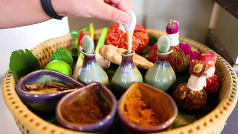 a hand arranges herbal ingredients in a basket for a traditional thai massage, showcasing vibrant colors and natural elements