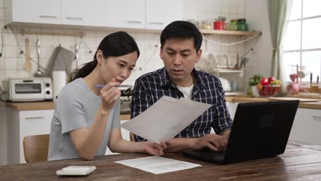 asian married couple discussing financial plans for the tax season in the dining room at home. they pointing at computer and looking at bills