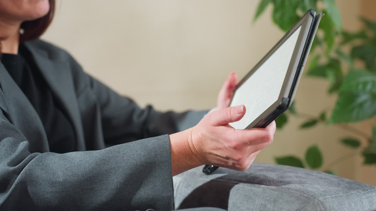 Businesswoman holding tablet with both hands while working remotely in indoor setting with green plant background, demonstrating focus, professionalism, and digital engagement in calm relaxed posture