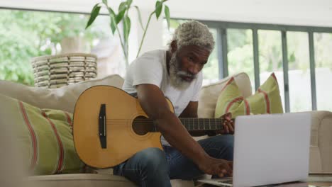 video of sad african american senior man playing the guitar and using laptop