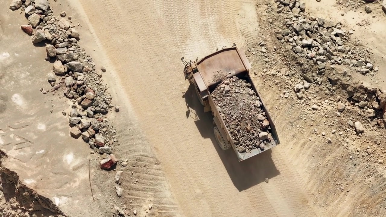 Luftfotos af et cementproduktionsanlæg med fokus på tungt maskineri i kalkstensbrud. Dumperlastbiler transporterer råmaterialer i et industrilandskab.