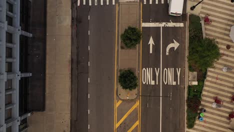 aerial top down view over a median between roads, as a few cars drive by below on the quiet roads