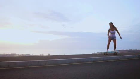 with the sun descending, a stunning and trendy skateboarder elegantly skates in shorts along a mountain road at sunset, with the mountains' stunning panorama in slow motion
