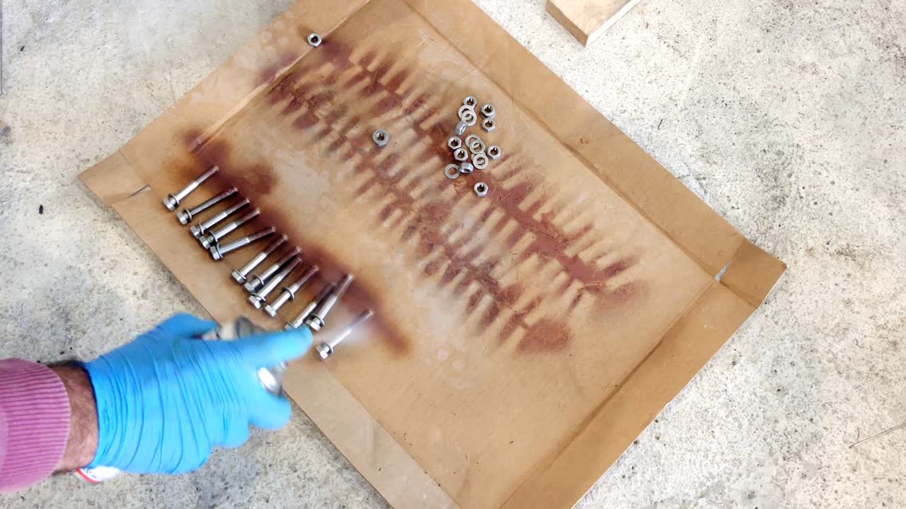 파란 라텍스 일회용 장갑으로 침투하는 기름 윤활유 스프레이로 볼트에서 녹을 청소하는 기계 노동자 손