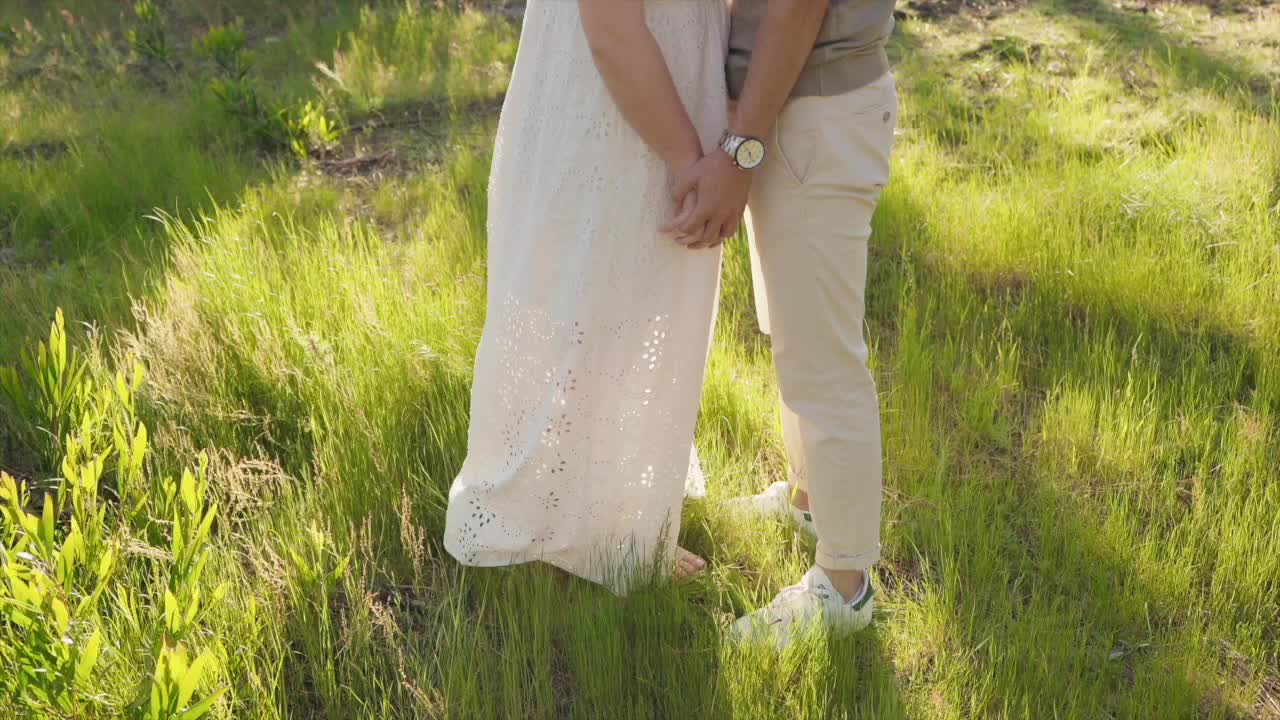 close up of couple’s hands and feet standing together in glowing meadow light