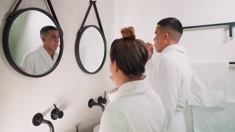 una pareja se cepilla los dientes en el baño del hotel. una joven familia de esposa y marido hace una rutina higiénica mirándose en los espejos en casa. una vida doméstica feliz